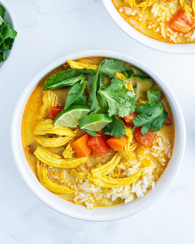 A bowl of chicken curry soup with rice, chicken, and topped with cilantro and basil.