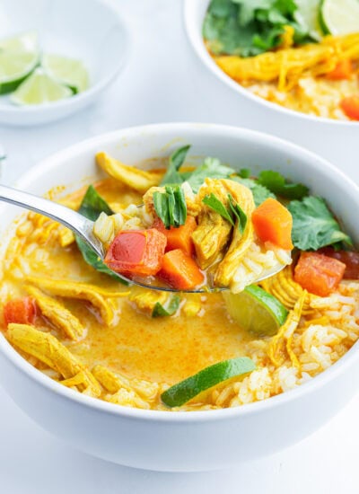 A spoonful of chicken curry soup, being held above a bowl of it.