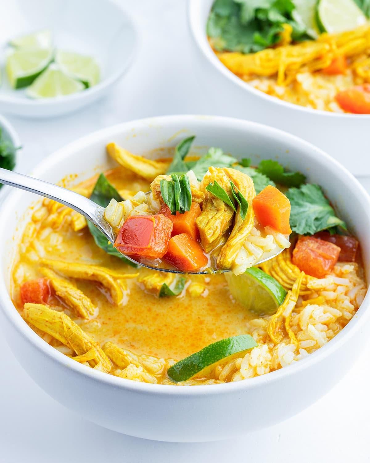 A spoonful of chicken curry soup, being held above a bowl of it.