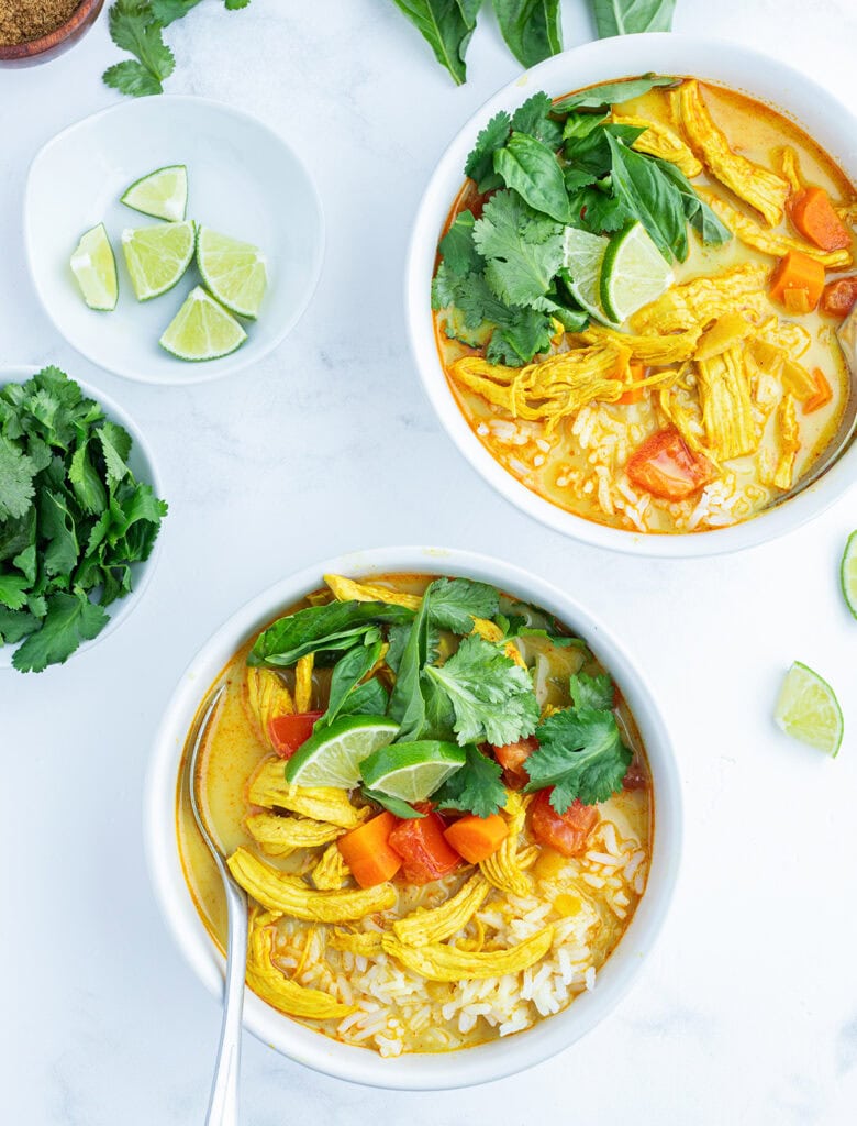 Two bowls of chicken curry soup with rice, chicken, and topped with cilantro and basil.