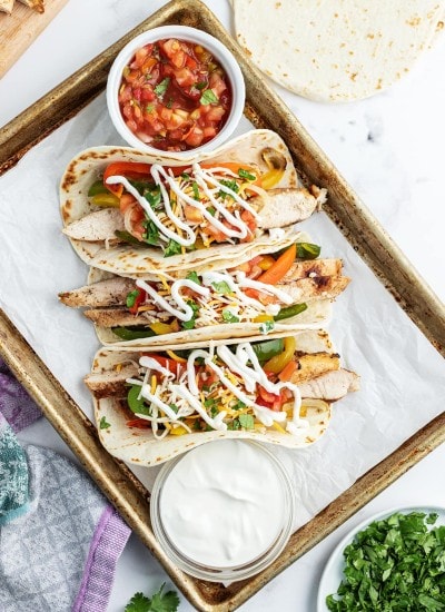 Three chicken fajitas loaded with salsa, sour cream, and cilantro.