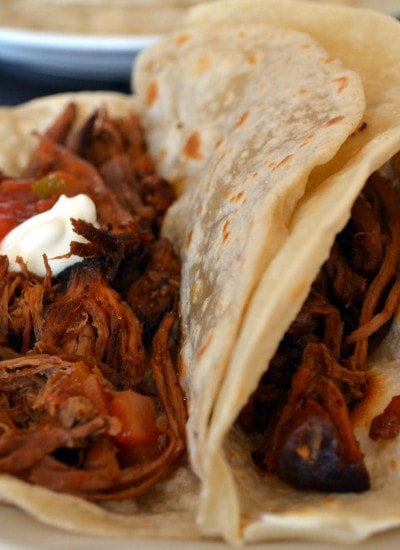 Close up view of shredded beef tacos in tortillas.