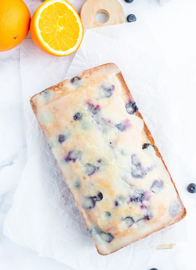 An above view of a loaf of blueberry bread topped with an orange glaze.