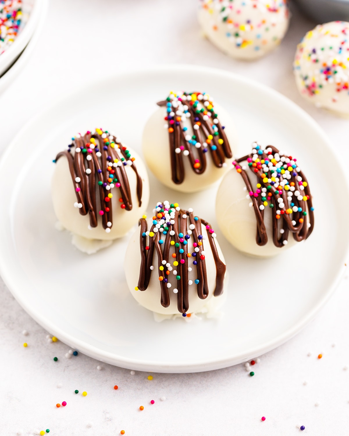 Four cake balls on a plate topped with a drizzle of melted chocolate and sprinkles.