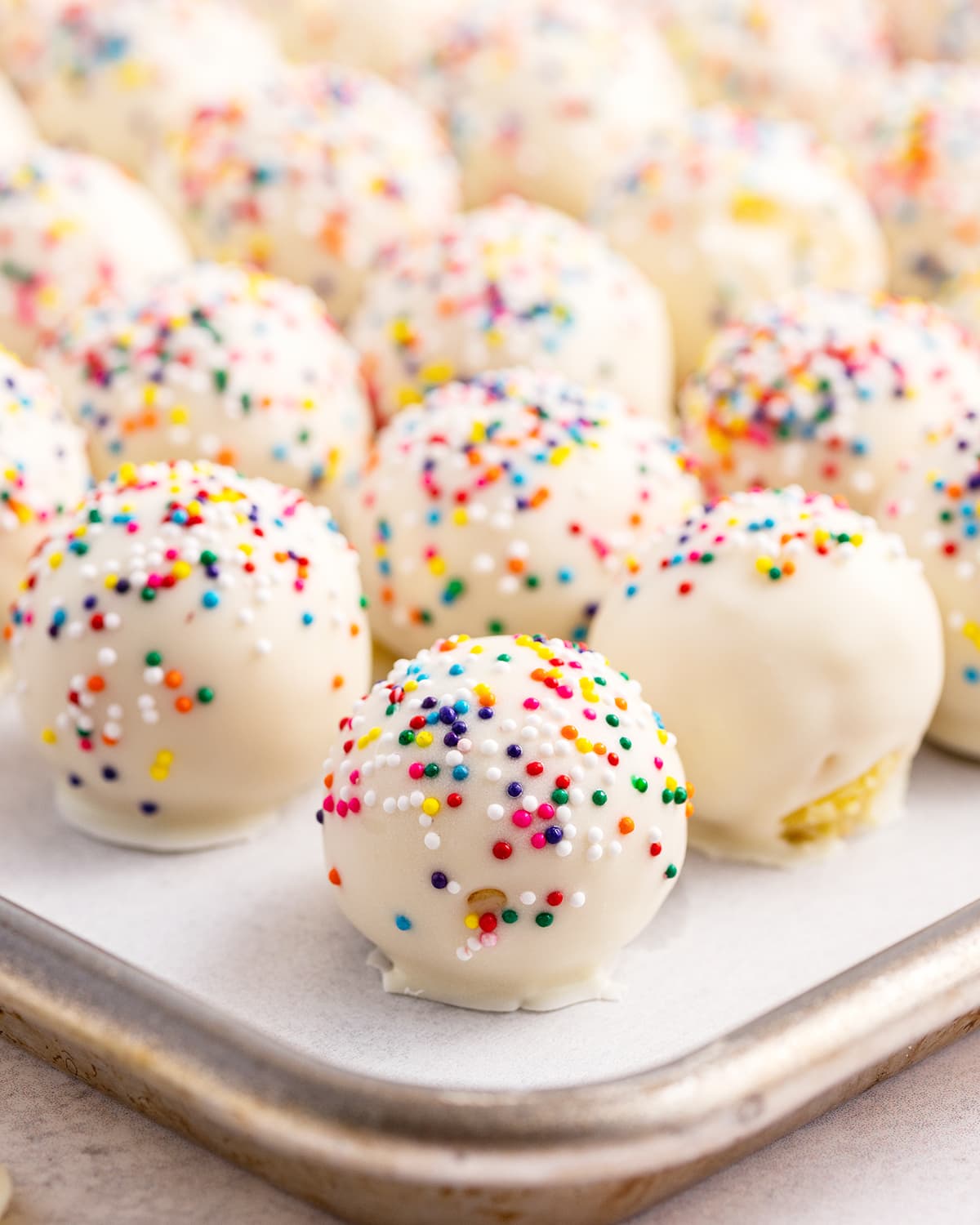 Cake balls pushed close together on a baking pan, they are topped with round rainbow colored sprinkles.
