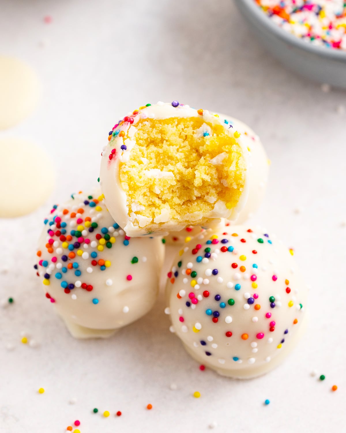 A pile of cake balls, the top ball has a bite out of it showing the yellow cake in the middle.