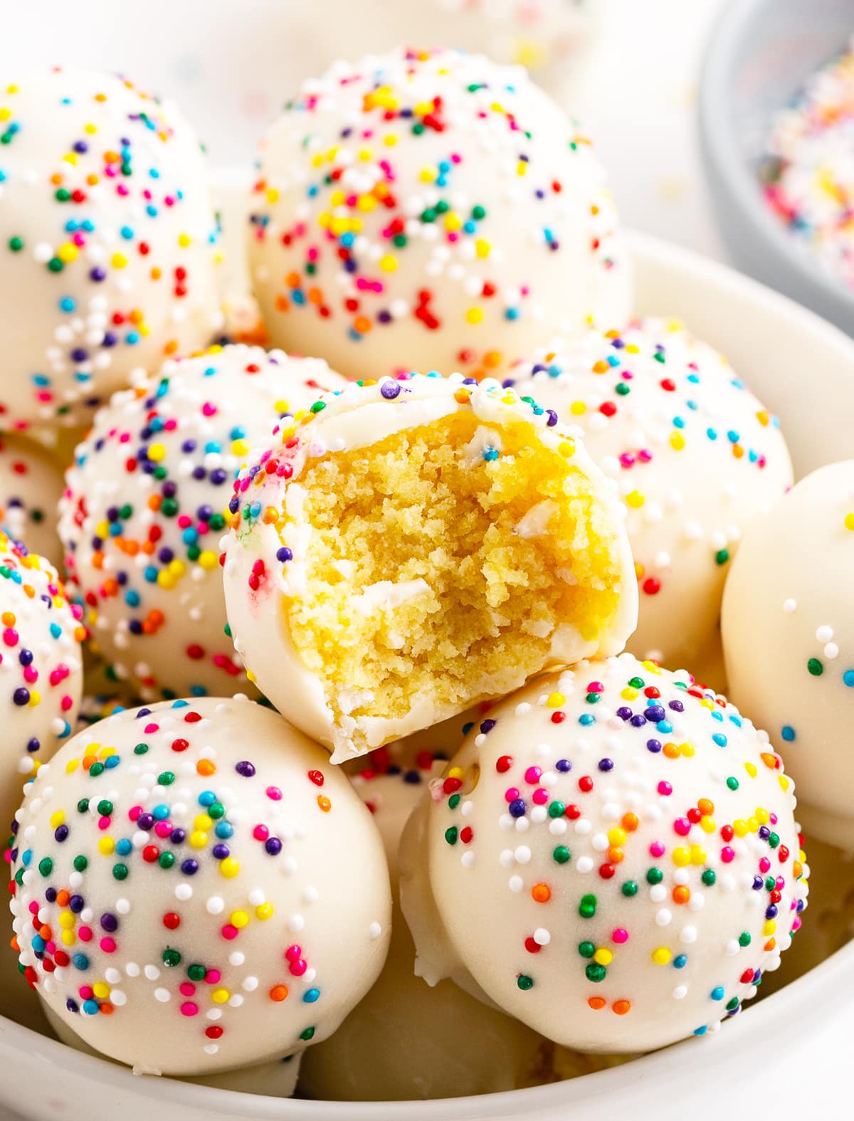 A bowl of cake balls, one has a bite out of it showing the yellow cake in the middle.