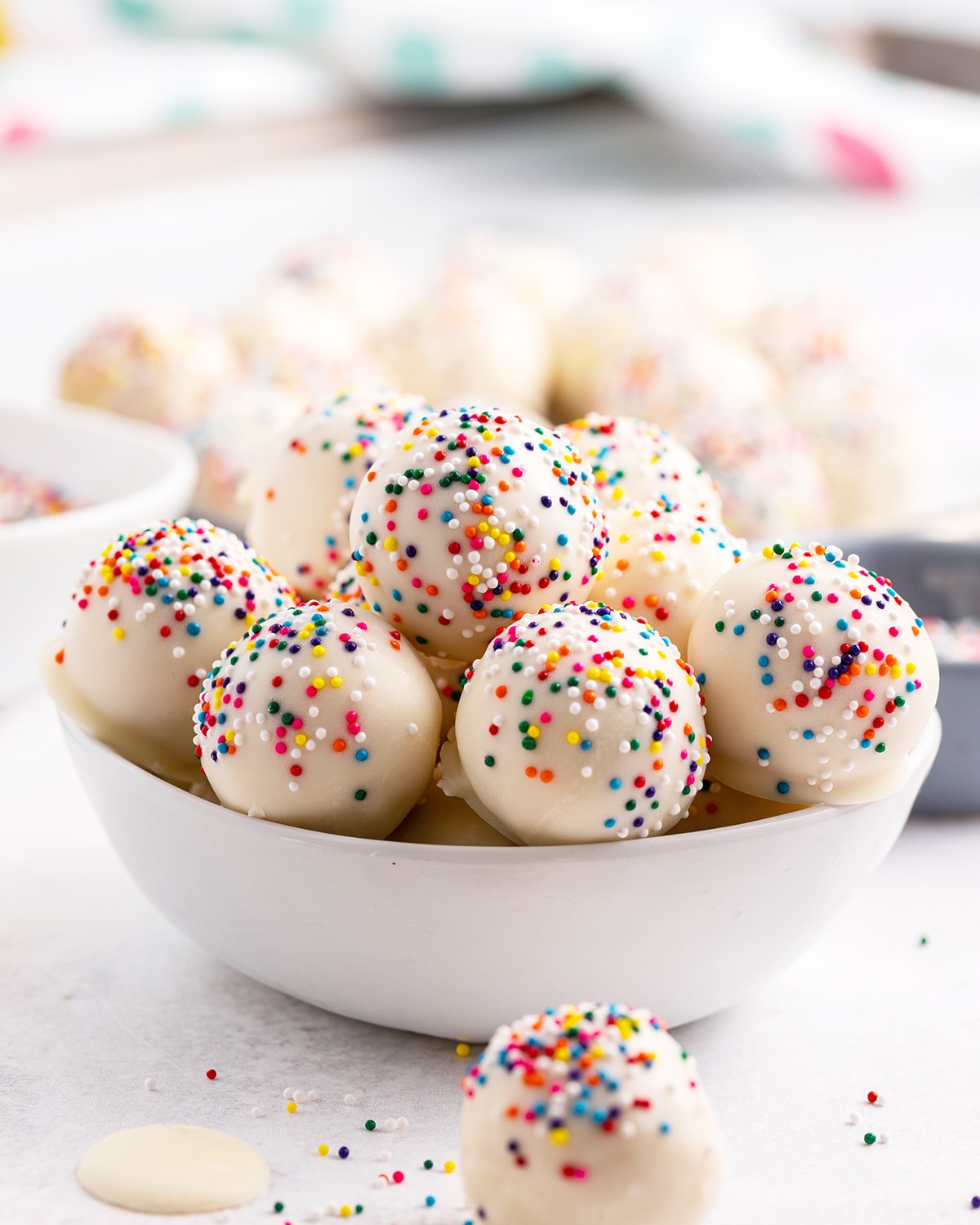 A white bowl full of white cake balls with rainbow sprinkles.