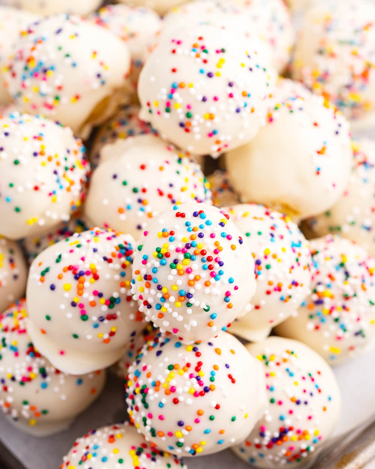 A close up of a bowl of cake balls covered in white chocolate and sprinkles.