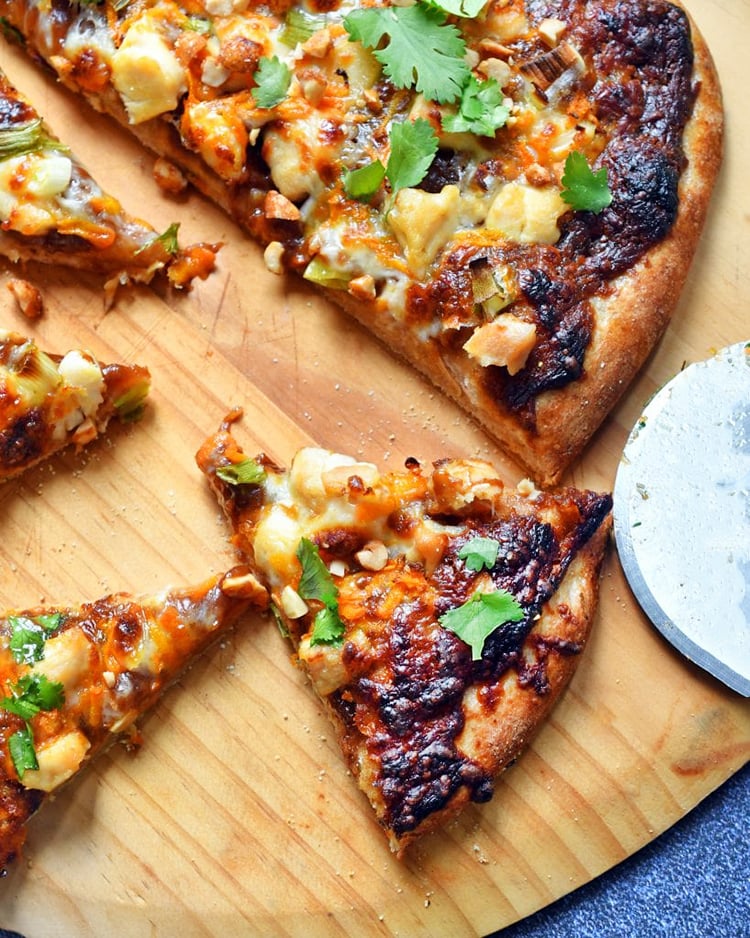 Angled view of thai chicken pizza on a wooden board.