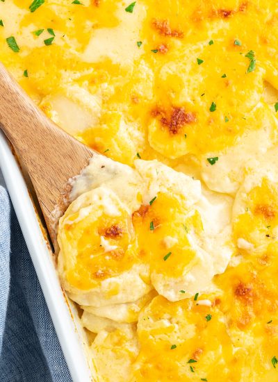 A close up of a spoonful of cheesy scalloped potatoes in a dish.