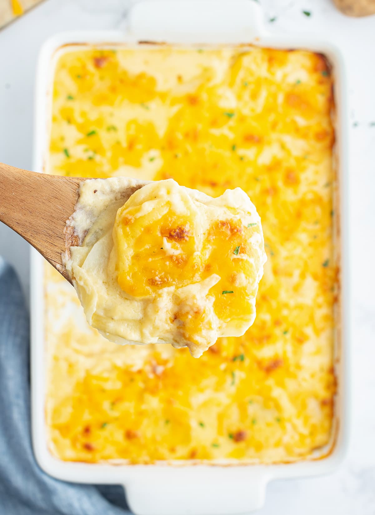 A spoonful of scalloped potatoes being held above a pan of potatoes.