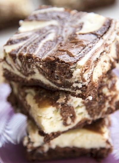 Cheesecake swirl brownies stacked on a purple plate.