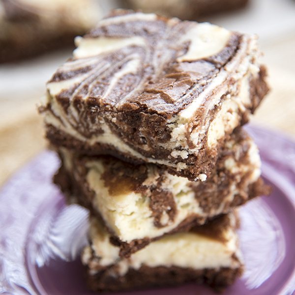 Cheesecake swirl brownies stacked on a purple plate.