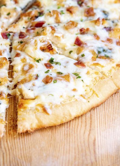 A slice of pizza topped with mozzarella cheese, chicken, bacon, and chopped parsley.