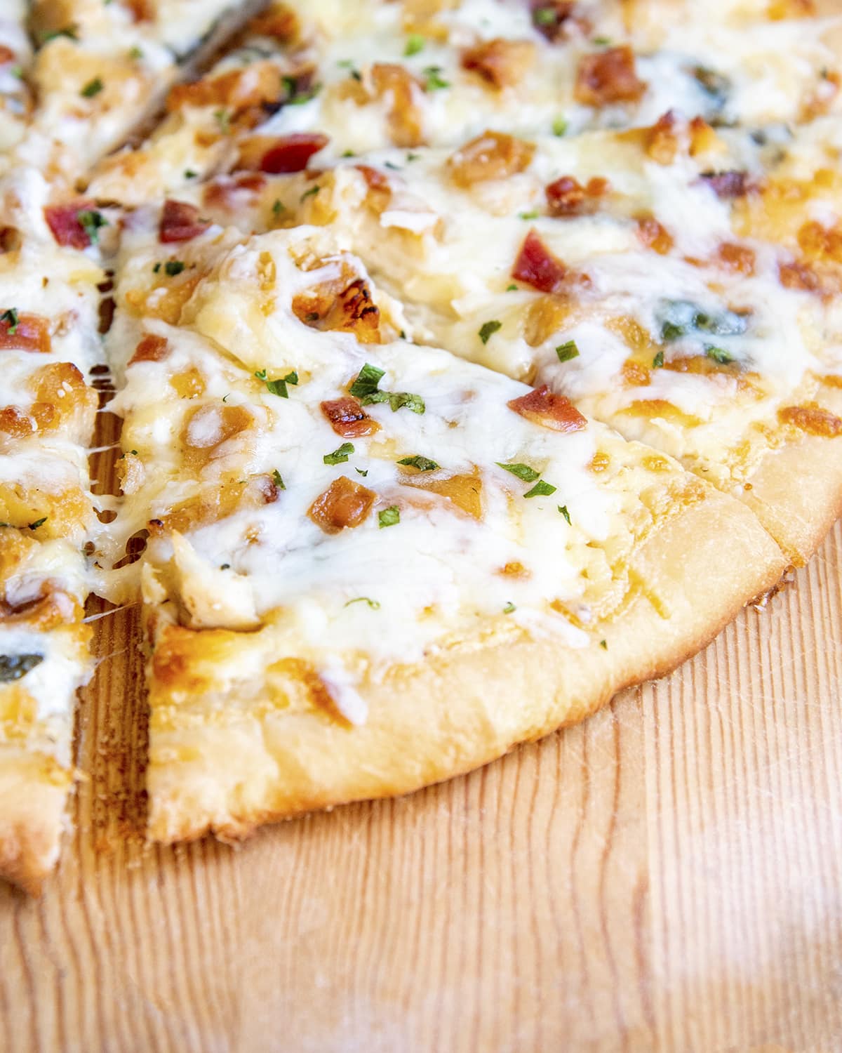 A slice of pizza topped with mozzarella cheese, chicken, bacon, and chopped parsley.
