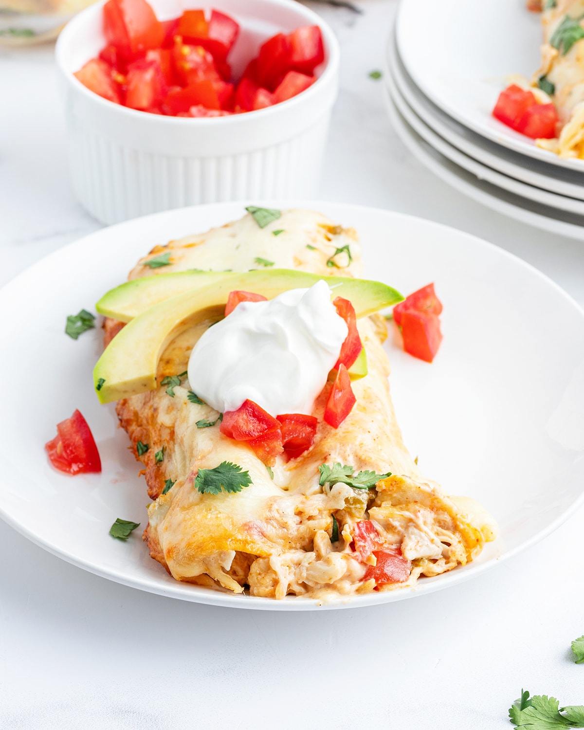 A plate of creamy chicken enchiladas topped with slices of avocado and sour cream.