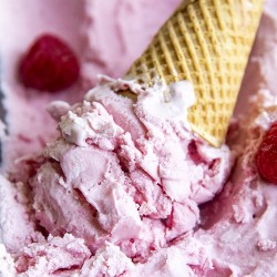 An upside down ice cream cone of pink raspberry ice cream, in a pan of raspberry ice cream.