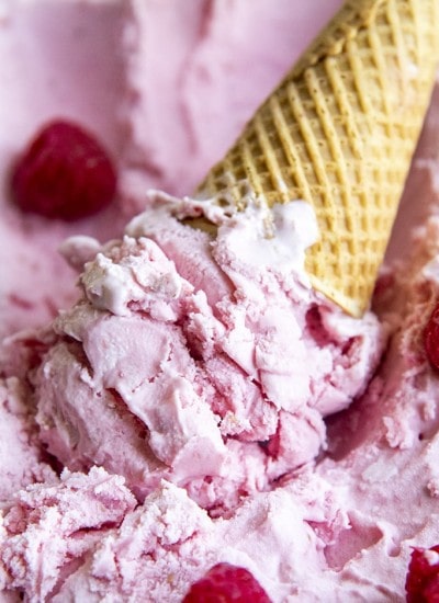 An upside down ice cream cone of pink raspberry ice cream, in a pan of raspberry ice cream.