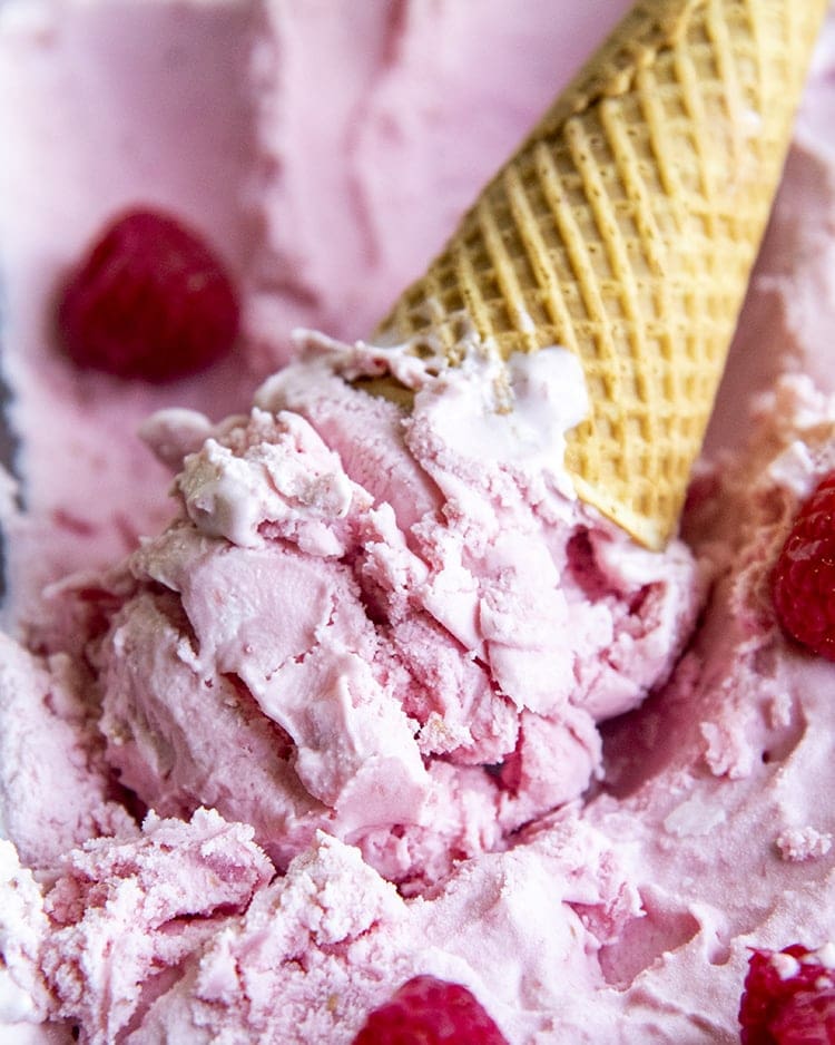 An upside down ice cream cone of pink raspberry ice cream, in a pan of raspberry ice cream.