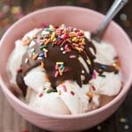 A bowl of vanilla ice cream topped with chocolate magic shell and sprinkles.
