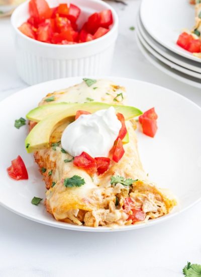 A plate of creamy chicken enchiladas topped with slices of avocado and sour cream.