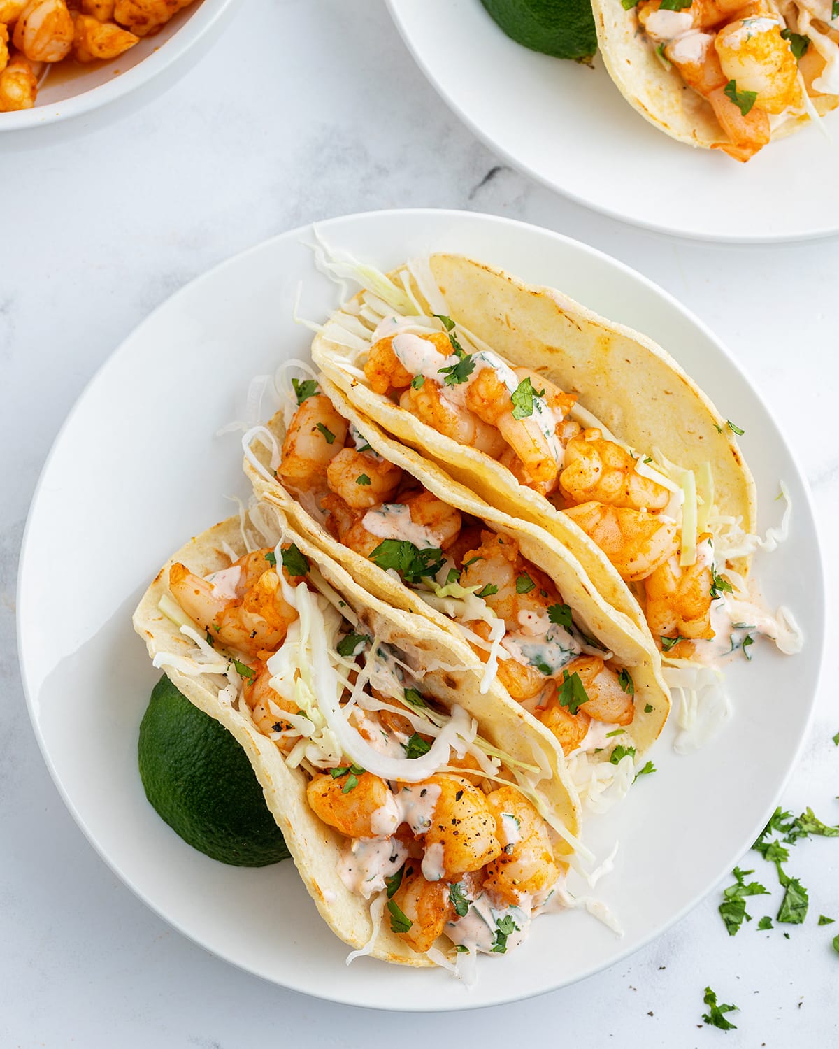 An overhead photo of a plate of three shrimp tacos topped with a cilantro yogurt sauce.