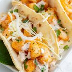 A close up of shrimp tacos topped with shredded cabbage and a greek yogurt sauce.