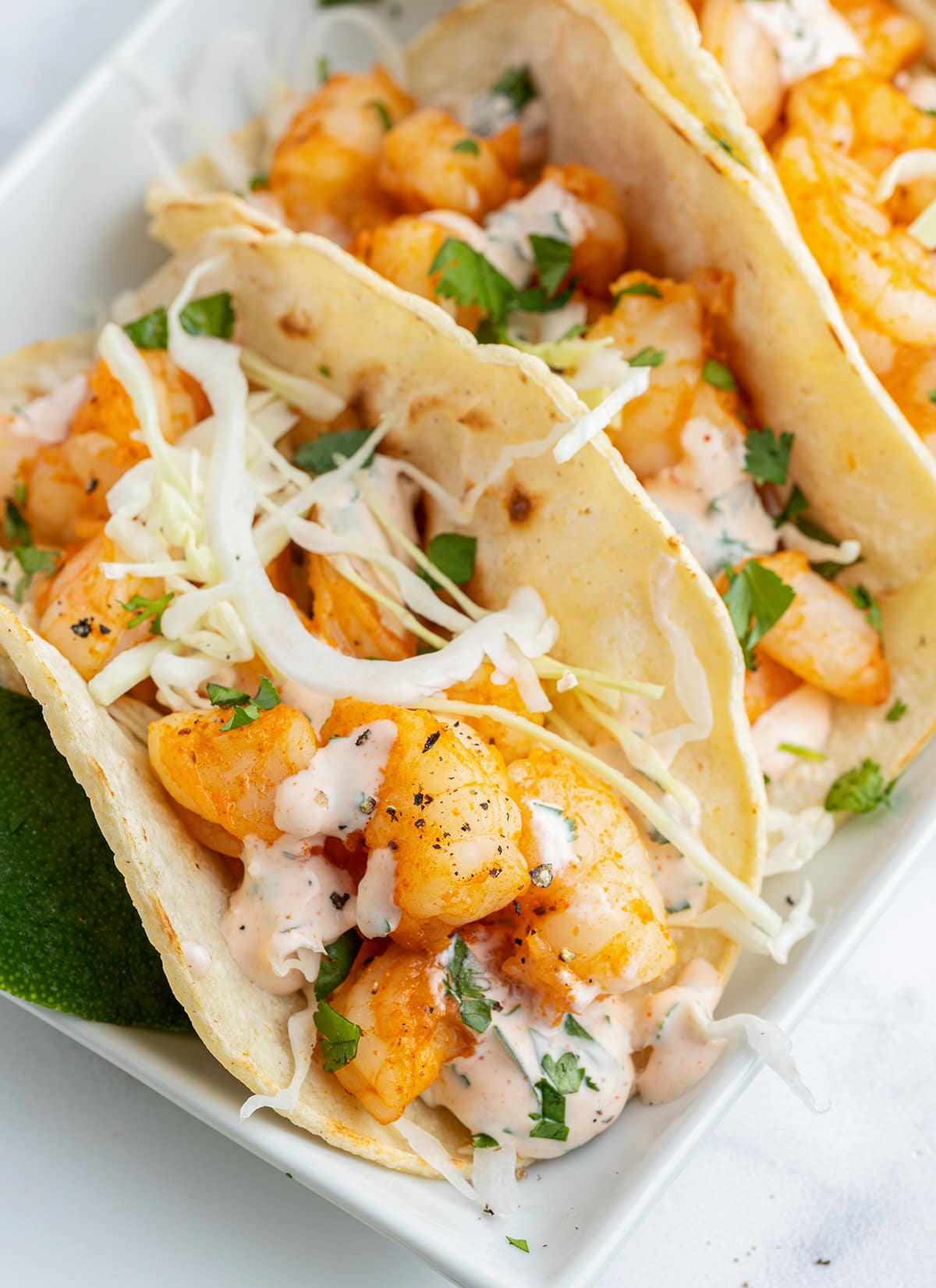 A close up of shrimp tacos topped with shredded cabbage and a greek yogurt sauce.