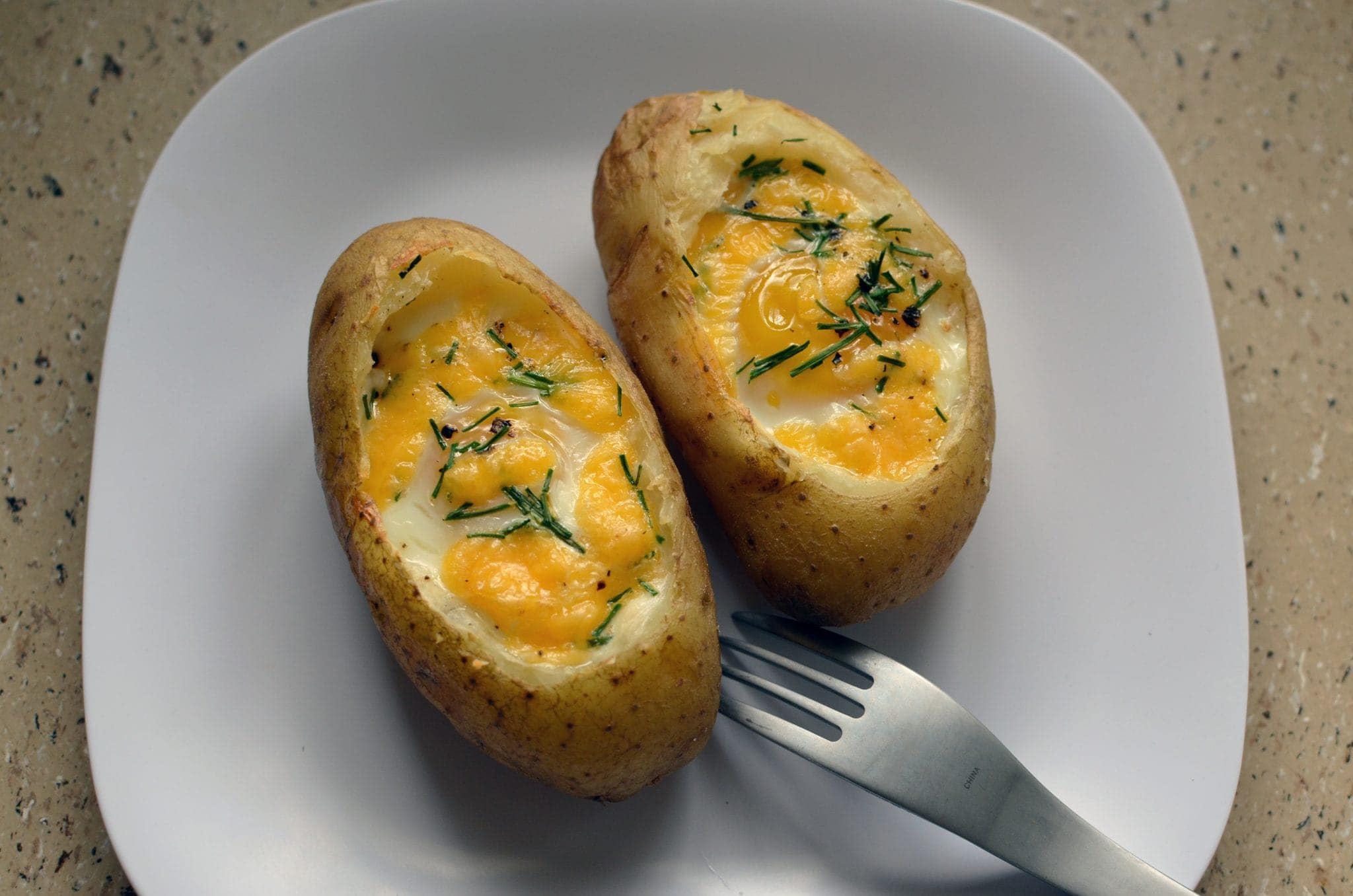 Top view of a baked egg in a baked potato on a white plate.