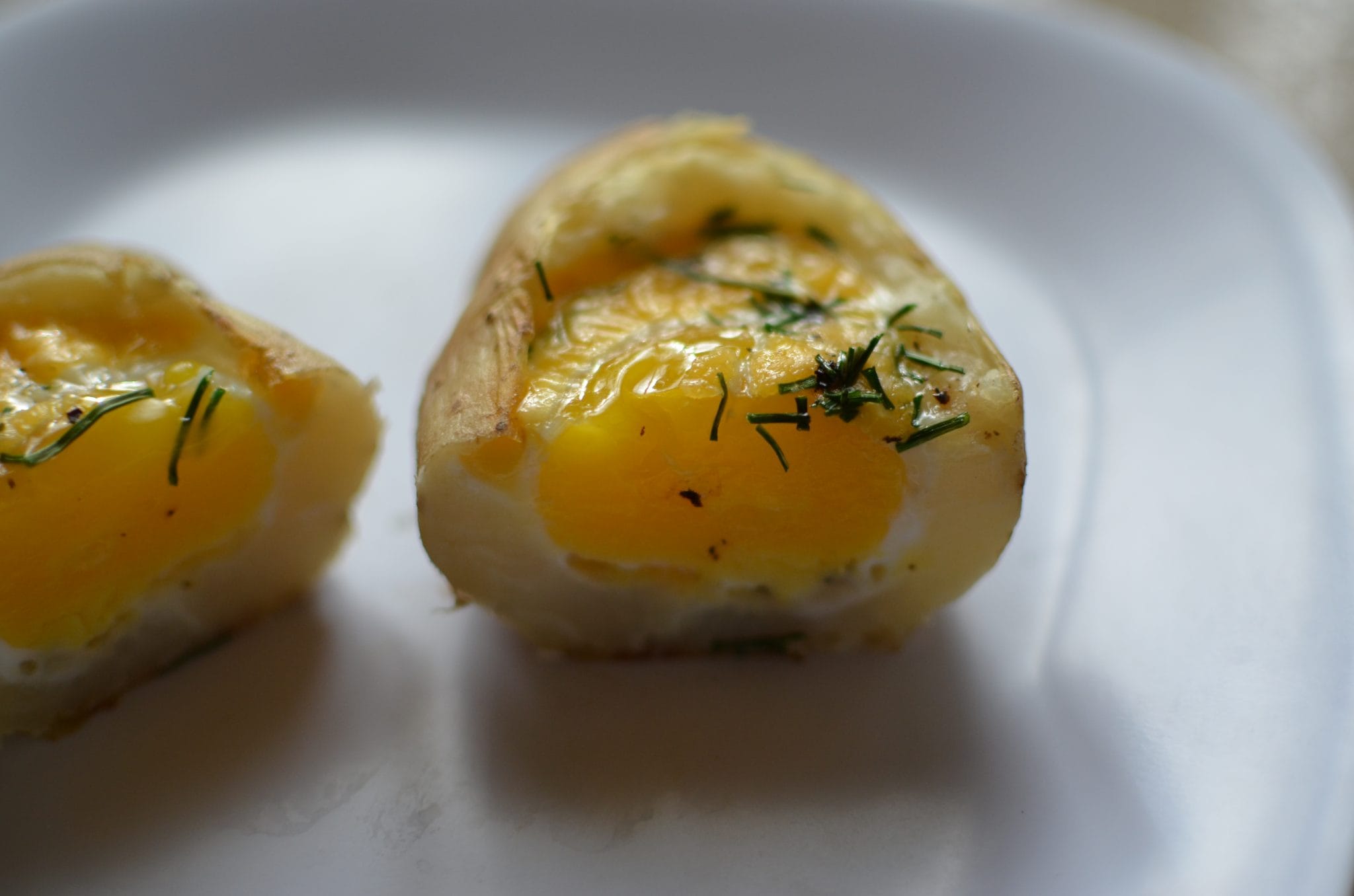 020 Front view of a split baked egg in a baked potato on a white plate.