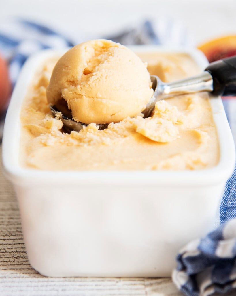 A scoop of an orange peach sherbet in an ice cream scoop.