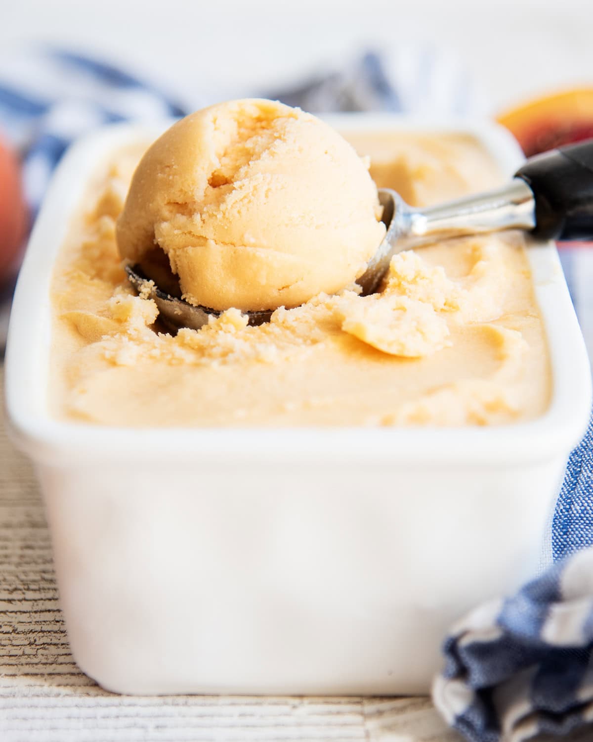 A scoop of an orange peach sherbet in an ice cream scoop.