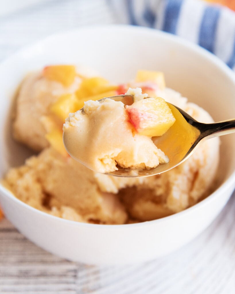 A spoonful of peach sherbet with a piece of fresh peach on it.