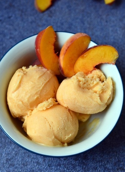 White bowl with 3 scoops of peach sherbet and 3 peach slices on blue background