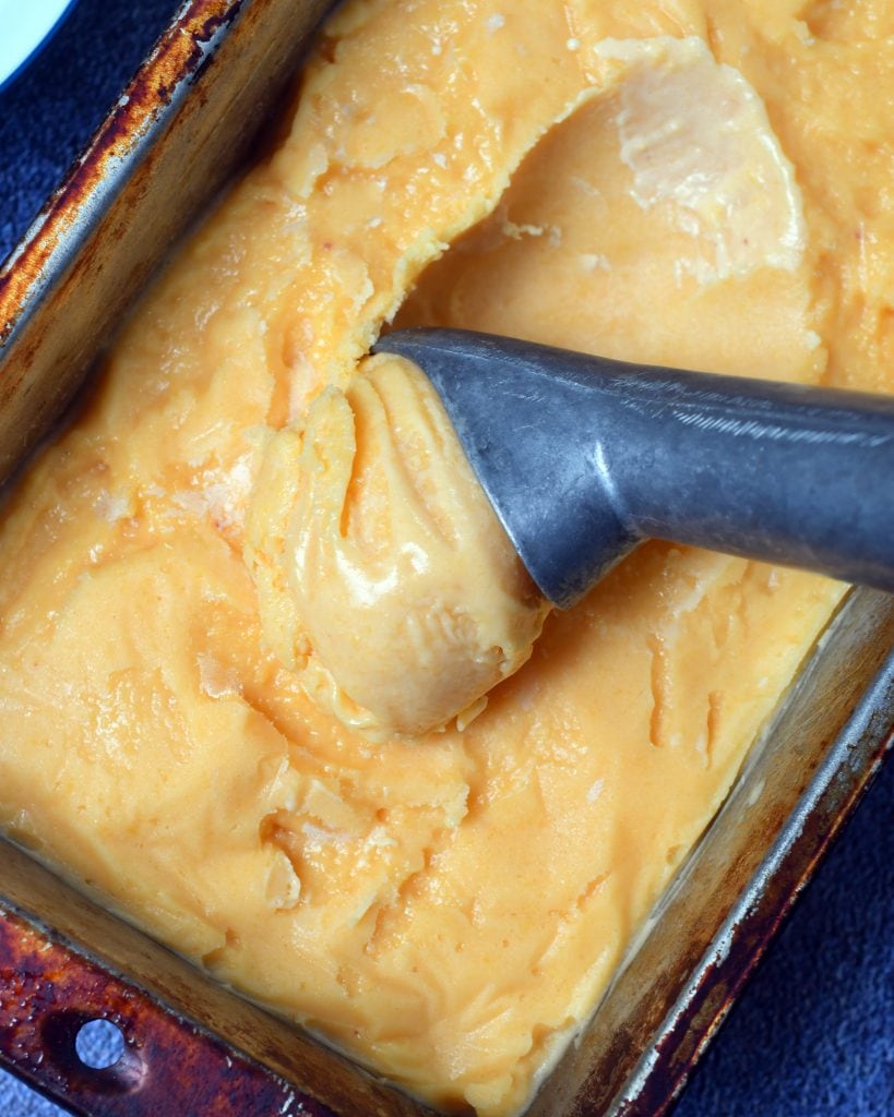 Peach sherbet being scooped by an ice cream scoop in a loaf pan