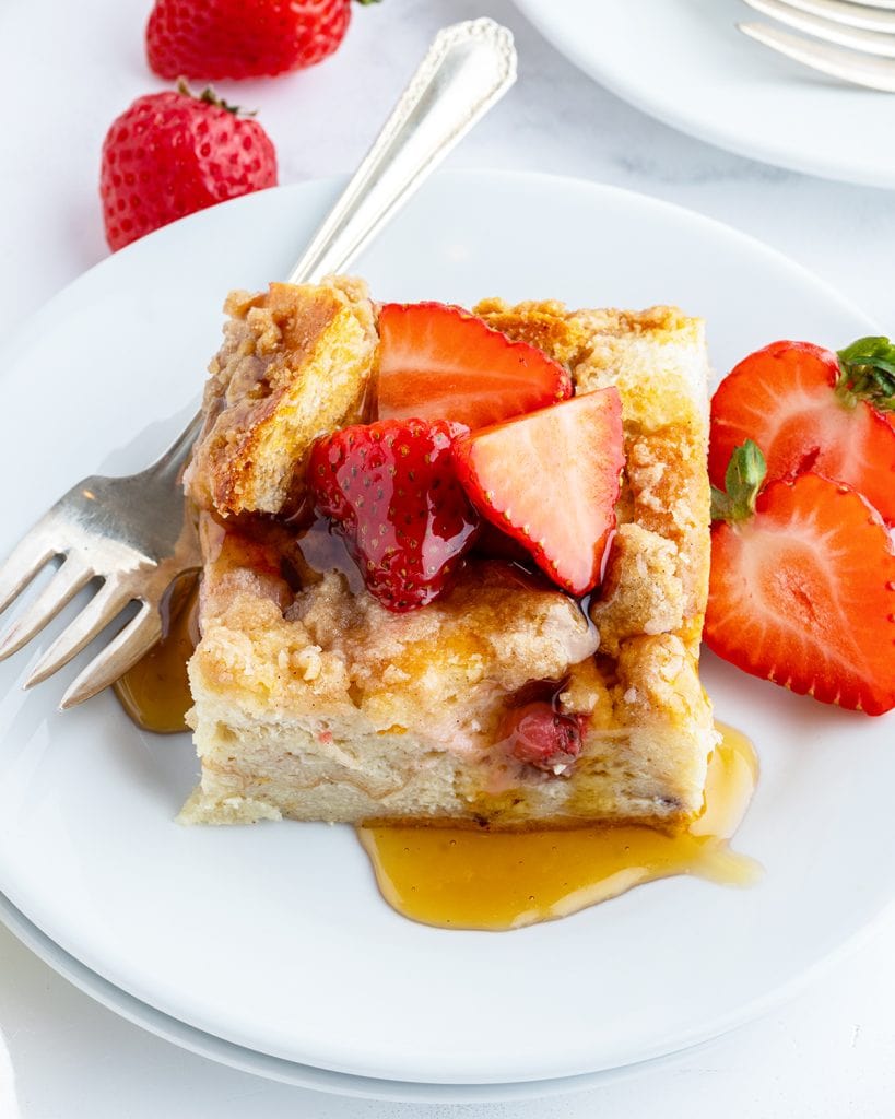A square serving of French toast casserole topped with strawberry slices and syrup.