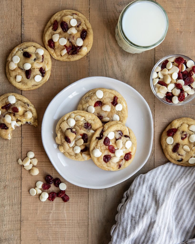 Three White Chocolate Cranberry Cookies with Macadamia Nuts on a plate next to a glass of milk.