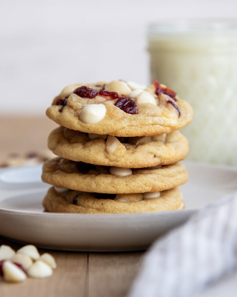 A stack of four white chocolate macadamia nut cookies with cranberries on a plate.