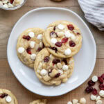 Three White Chocolate Cranberry Cookies with Macadamia Nuts on a plate next to a glass of milk.