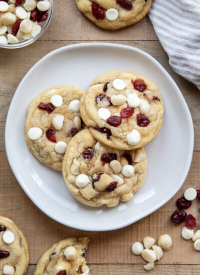 Three White Chocolate Cranberry Cookies with Macadamia Nuts on a plate next to a glass of milk.