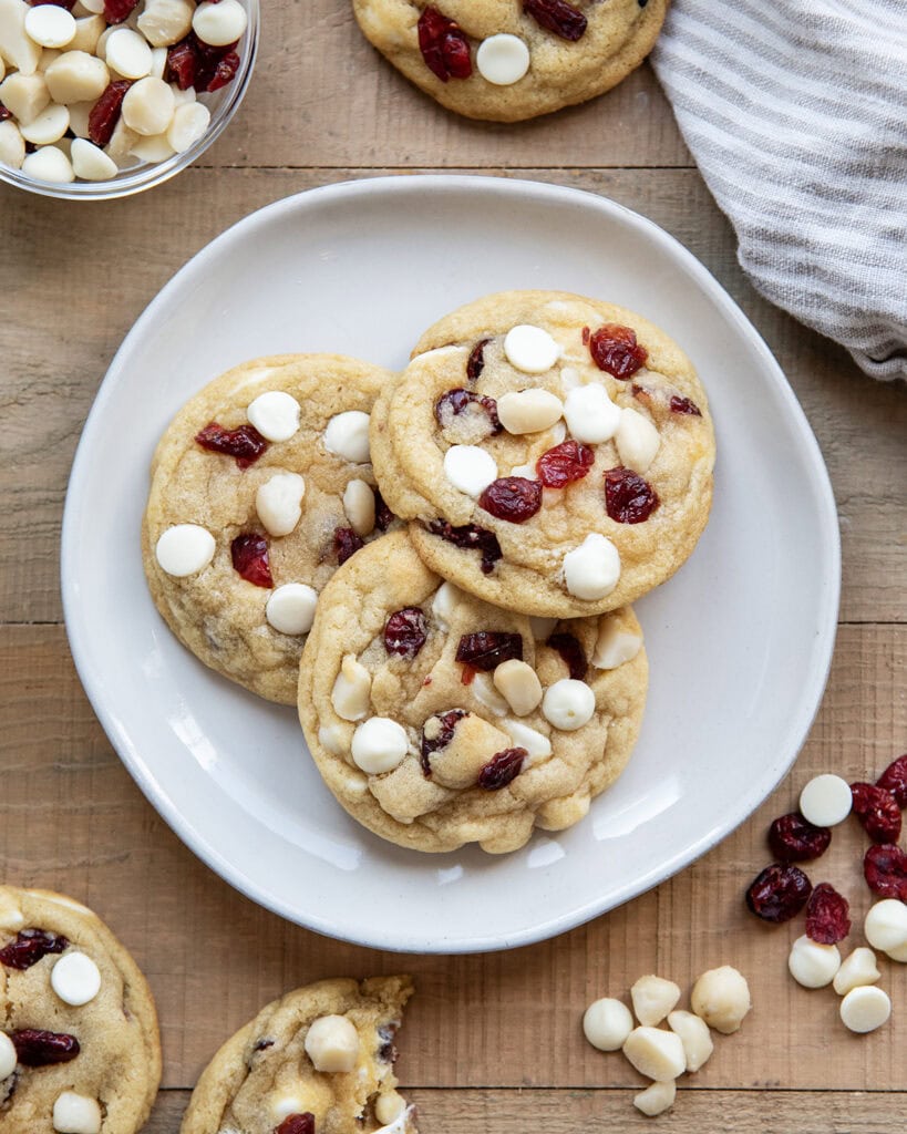Three White Chocolate Cranberry Cookies with Macadamia Nuts on a plate next to a glass of milk.