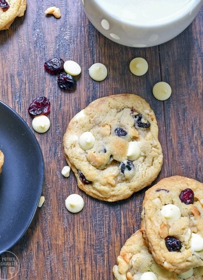 Top view of white chocolate, macadamia nut, and cranberry cookies on a wood board.