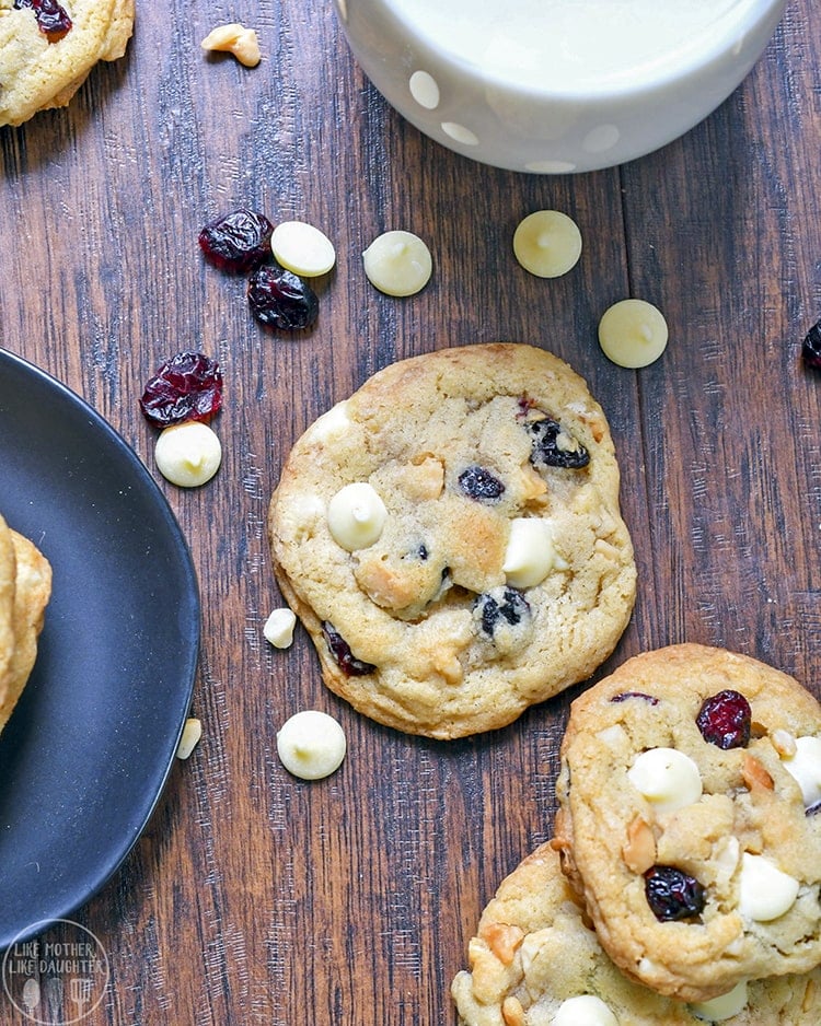 Top view of white chocolate, macadamia nut, and cranberry cookies on a wood board.