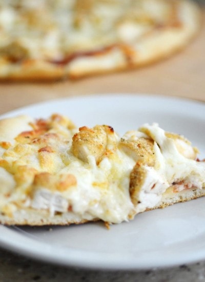 Angled view of chicken parmigiana pizza on a white plate.