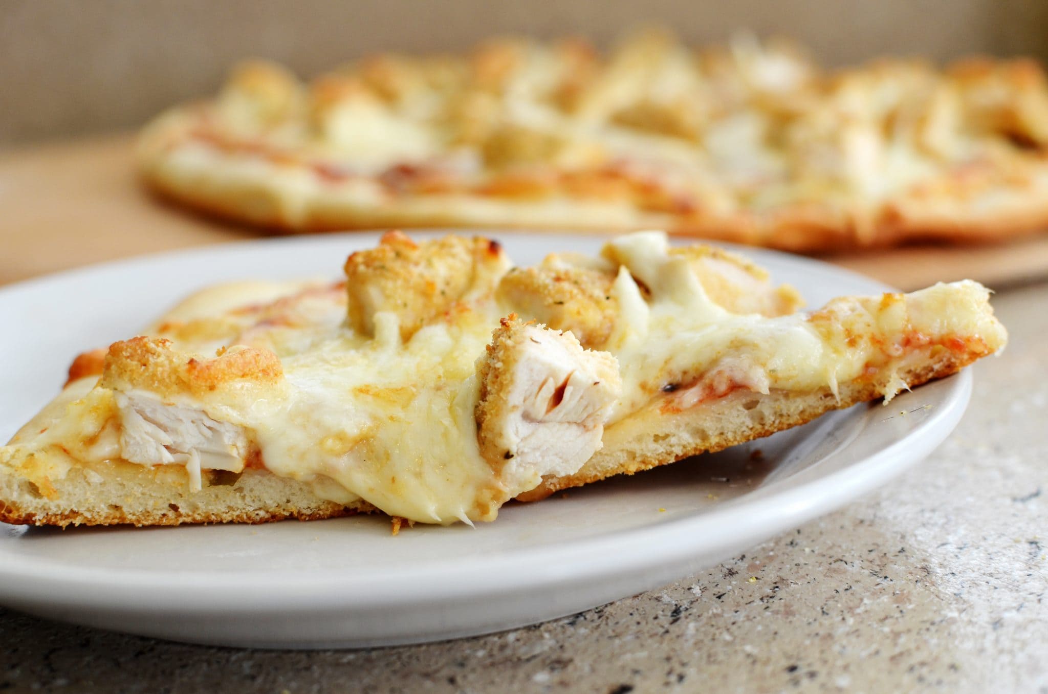 077 Front view of a slice of parmesan chicken pizza on a white plate.