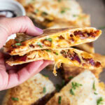 A hand holding two pieces of BBQ Chicken Quesadilla.