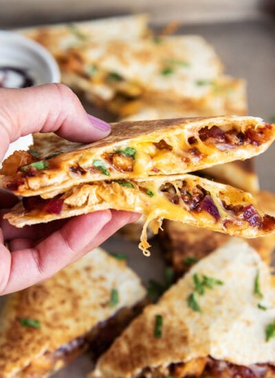 A hand holding two pieces of BBQ Chicken Quesadilla.