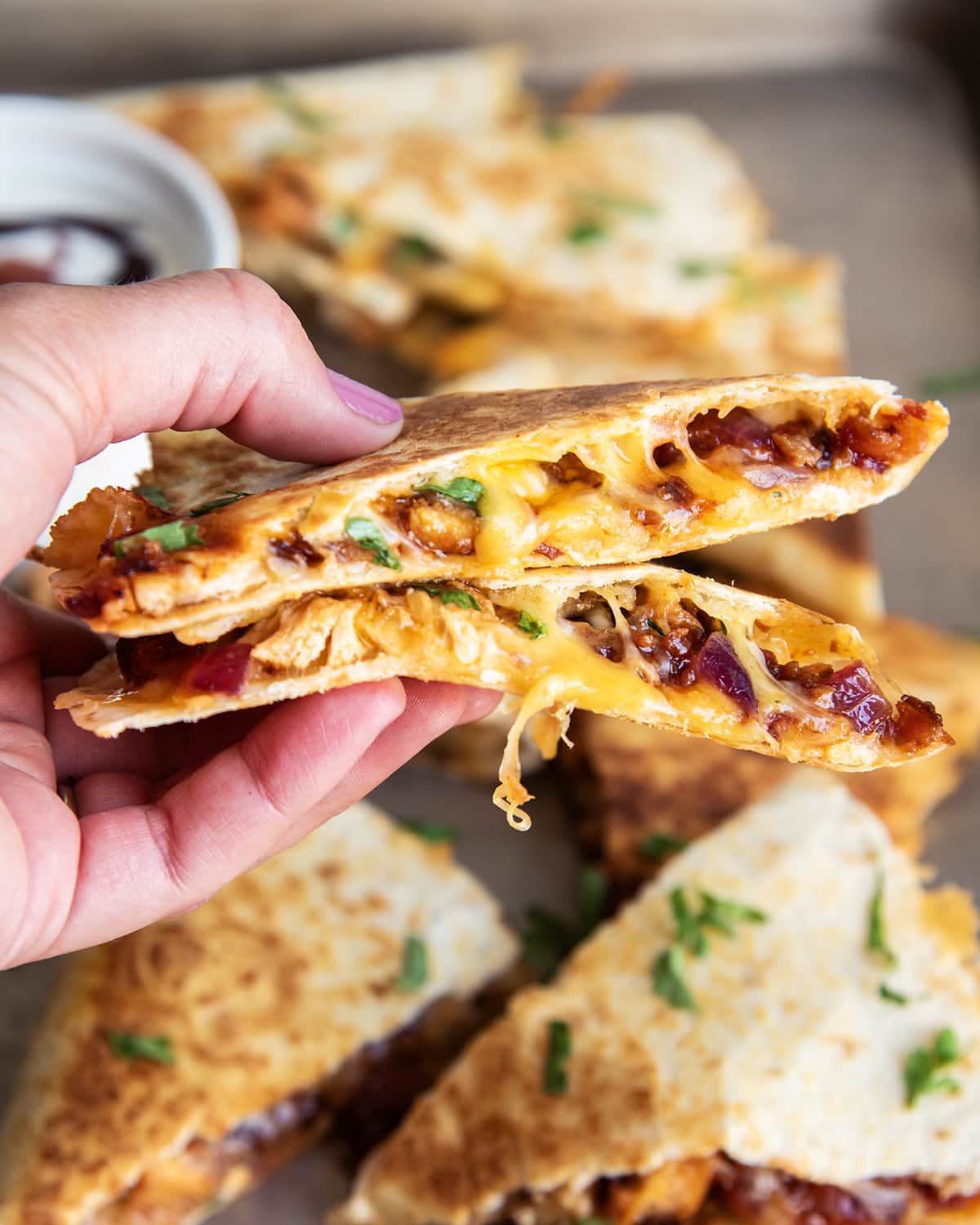 A hand holding two pieces of BBQ Chicken Quesadilla.