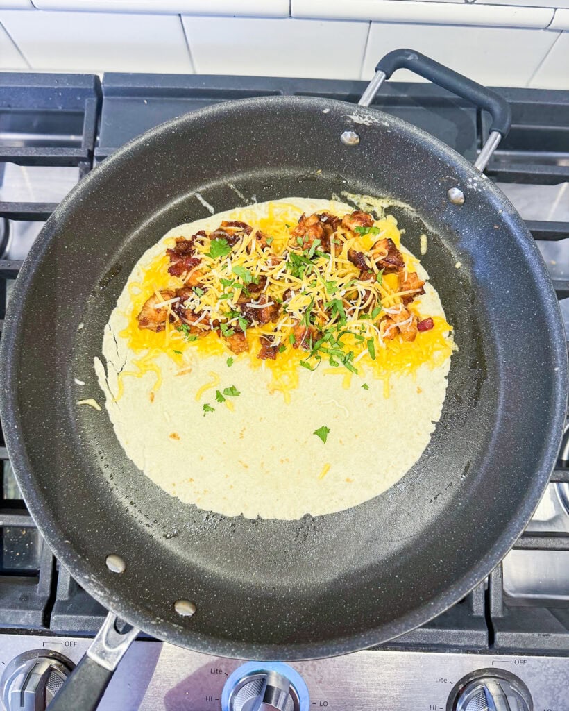 A tortilla topped with cheese, bbq chicken mix, and cilantro on half.